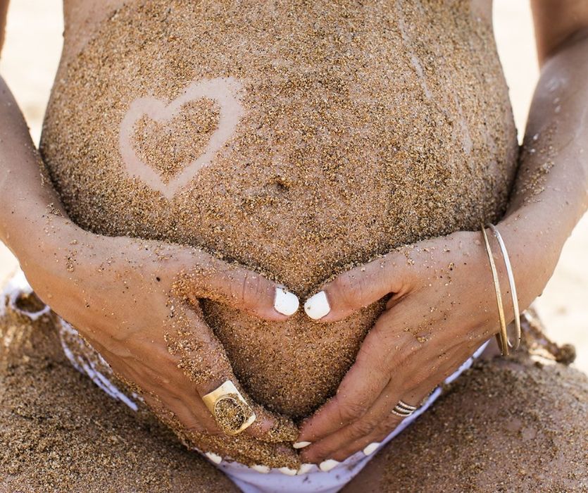 baby bump covered in sand with a heart traced on her belly