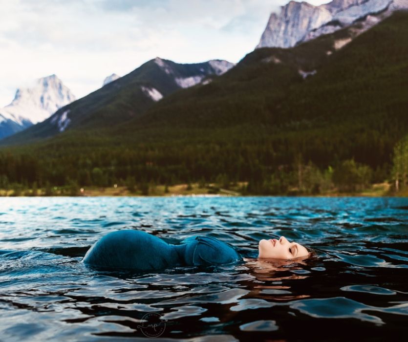 femme enceinte flottant sur le dos dans un lac à flanc de montagne