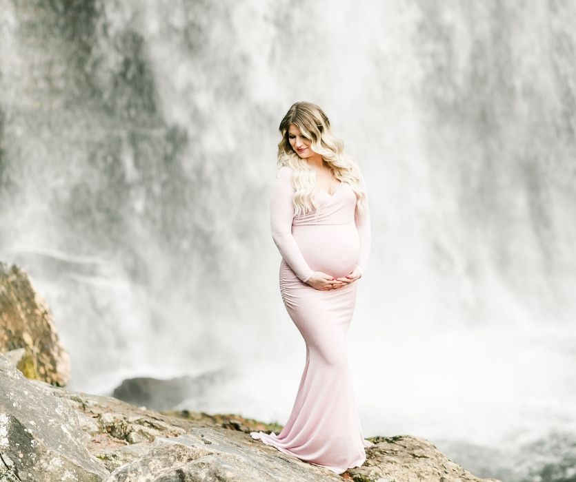 pregnant woman in a long pink dress next to a waterfall