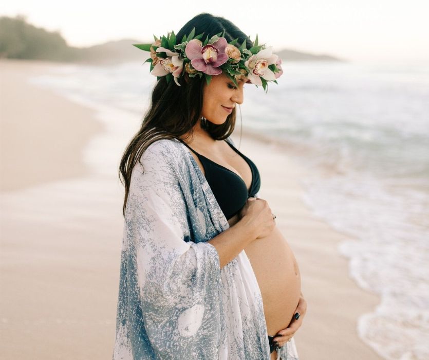 pregnant woman wearing a flower crown next to the ocean