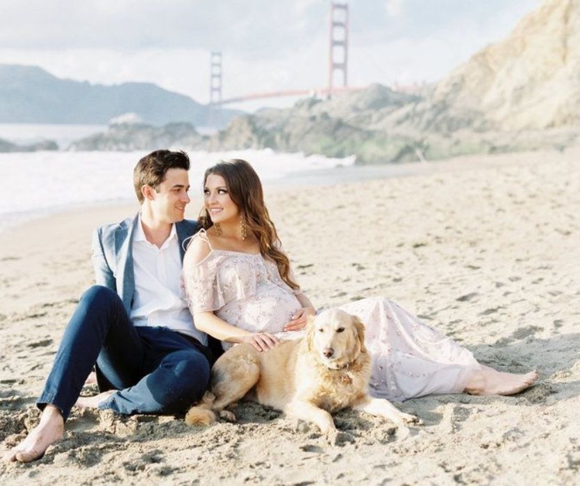 expectant couple with dog on the beach in front of bridge