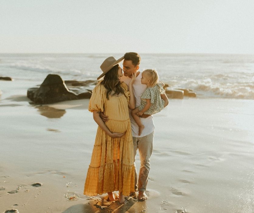 expectant couple with toddler about to kiss on the beach