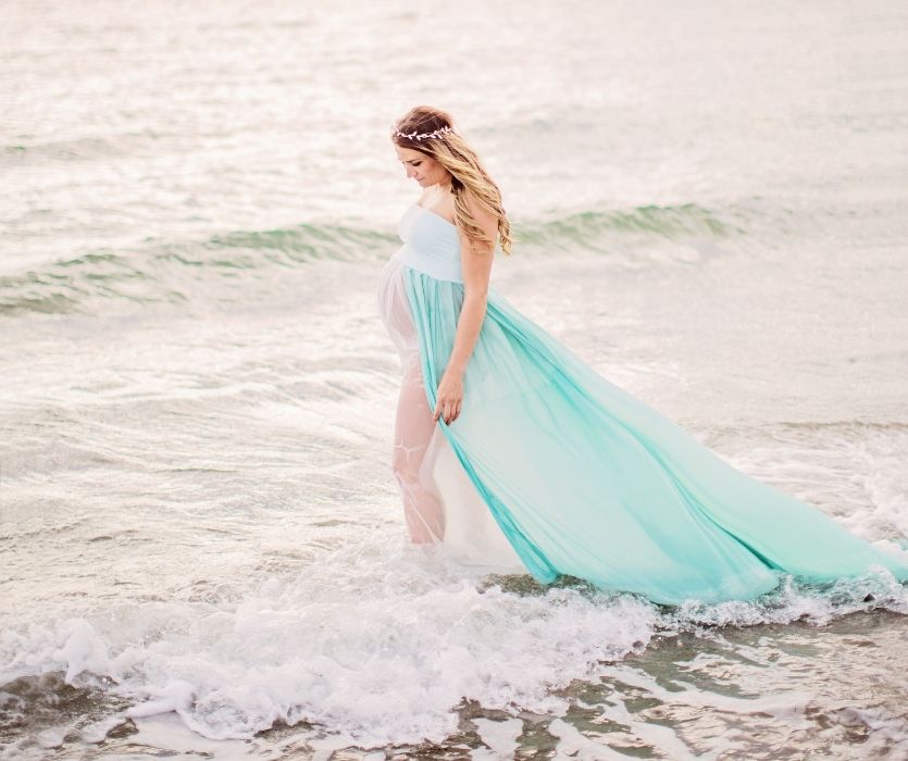 pregnant woman in a light blue dress walking in the surf