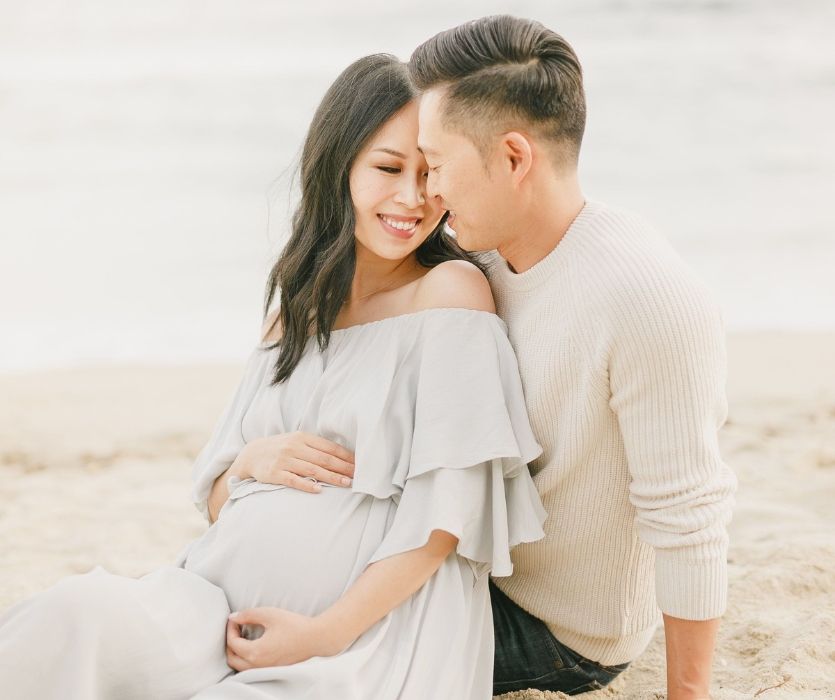 man and his pregnant wife sitting on the beach