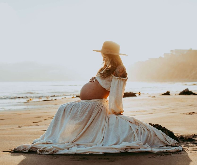 pregnant woman in a straw at in a long skirt on the beach at sunset