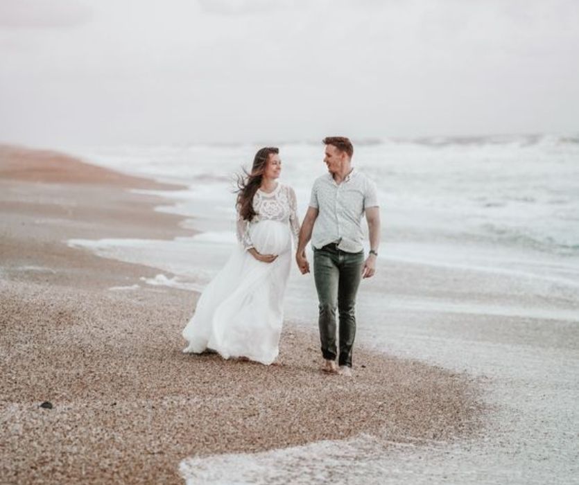 couple expecting a baby walking hand in hand on the beach