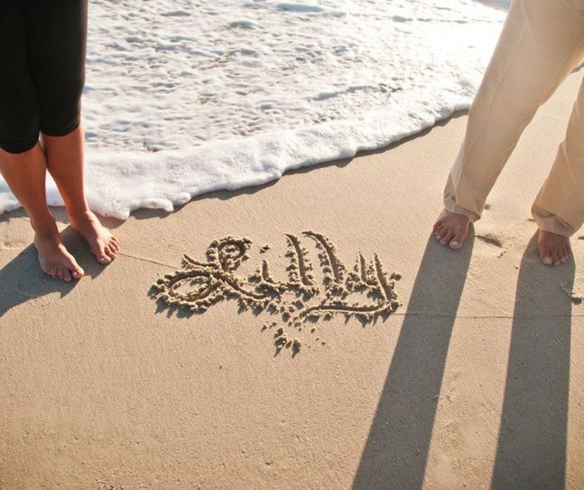 couple's feet next to the name Lilly written in the sand