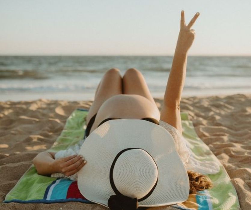 pregnant woman in at lying on the beach holding up a peace sign