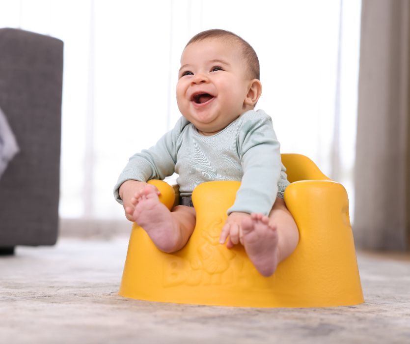 baby sitting in yellow bumbo on the floor