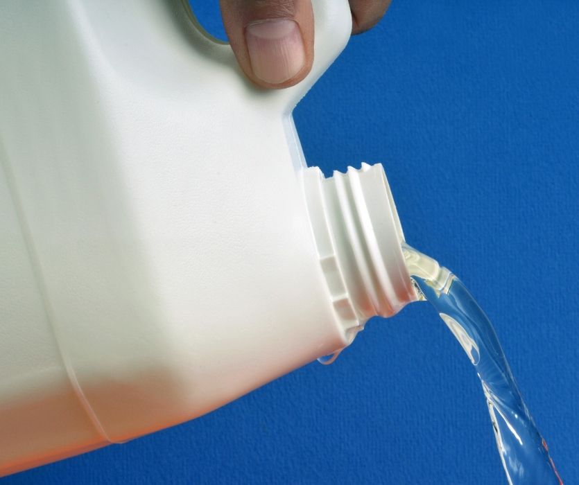 hand pouring detergent into a white jug