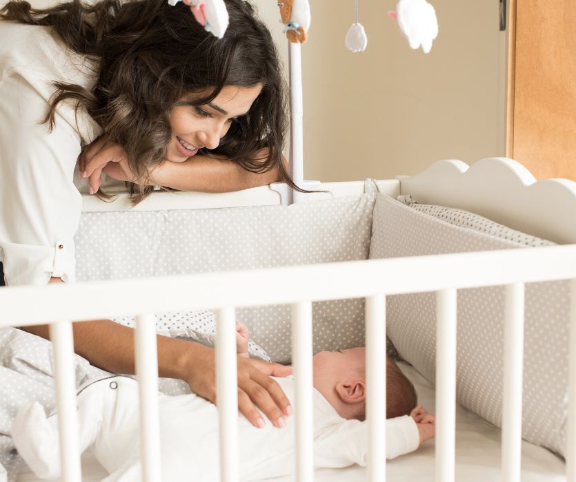 mom with her hand on her baby in a crib with bumpers