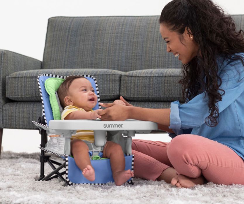 mom sitting on living room floor with her baby in a portable travel high chair