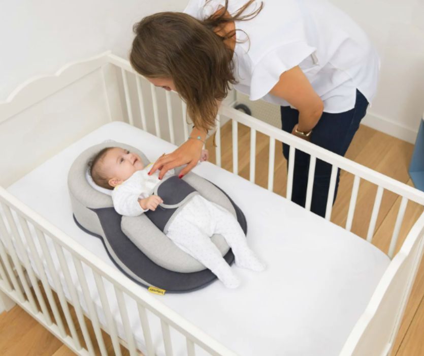 mom with her hand on her baby in a crib with a positioner