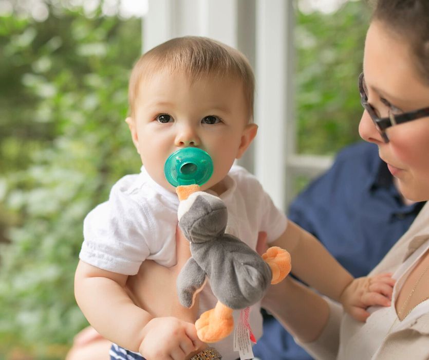 mom holding baby with a penguin wubbanub in their mouth