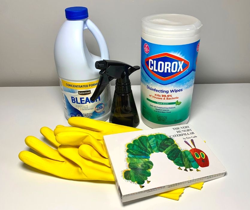 bleach container, spray bottle, board book, disinfecting wipes and yellow rubber gloves