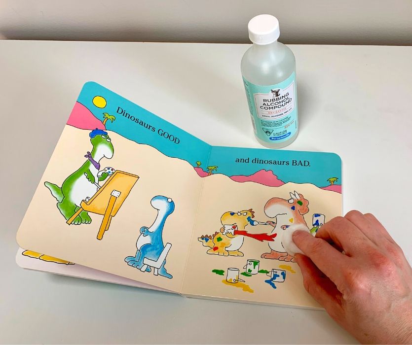 hand using cotton ball with rubbing alcohol to clean a child's book