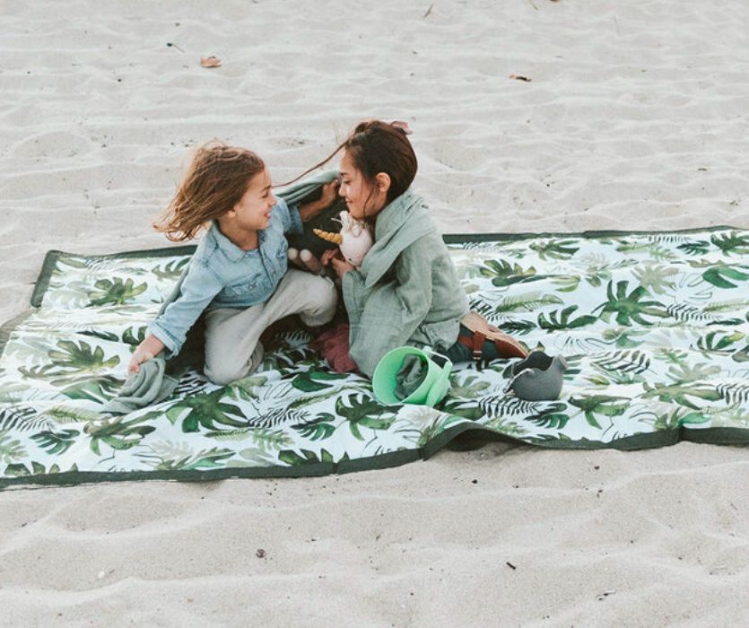 hai đứa trẻ ở bãi biển trên một tấm chăn lớn trên bãi biển