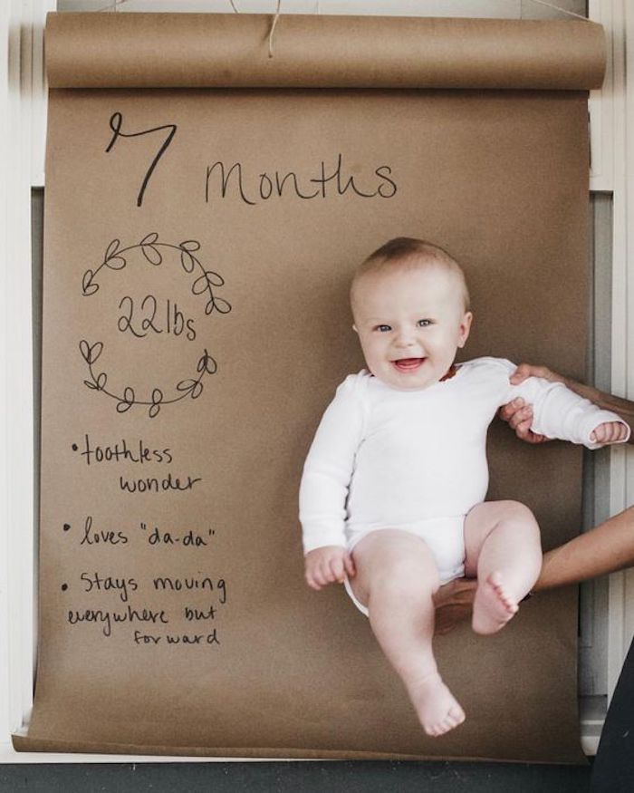 baby held up against butcher paper backdrop with 7 month stats written on it