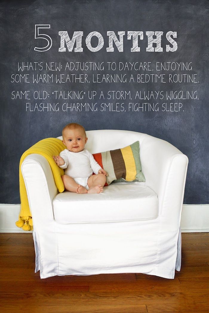 baby sitting in white chair in front of a chalkboard wall with lettering