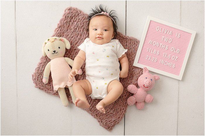 baby girl next to pink letterboard and pink stuffed toys