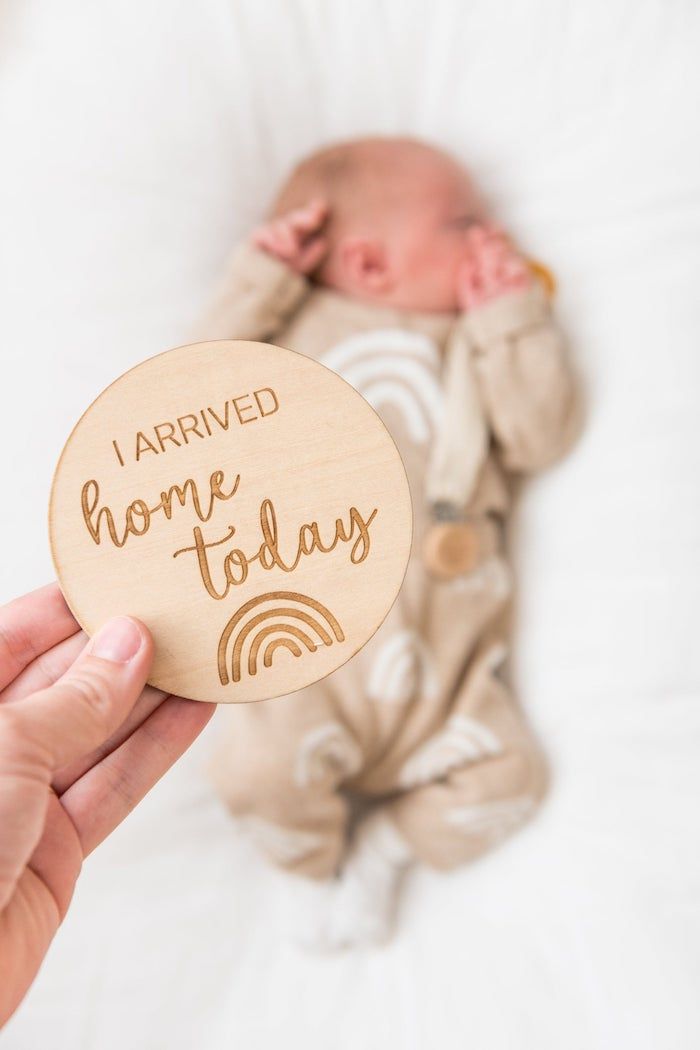 hand holding wooden disk that says I arrived home today in front of newborn baby