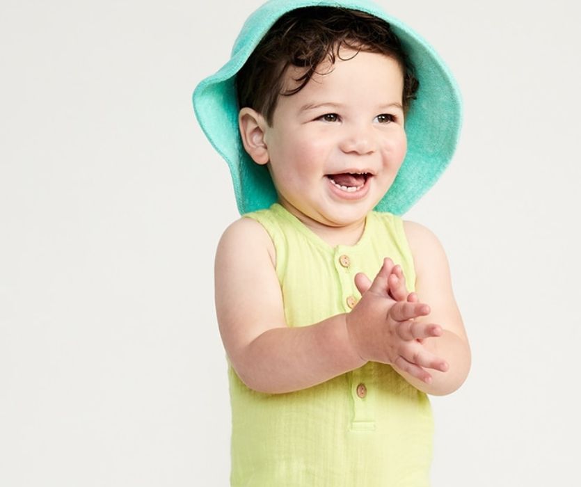 smiling child wearing yellow romper and green hat