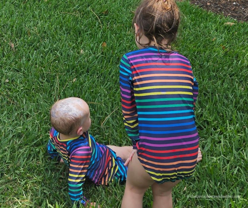 Two kids in rainbow stripe swimsuits playing in the grass