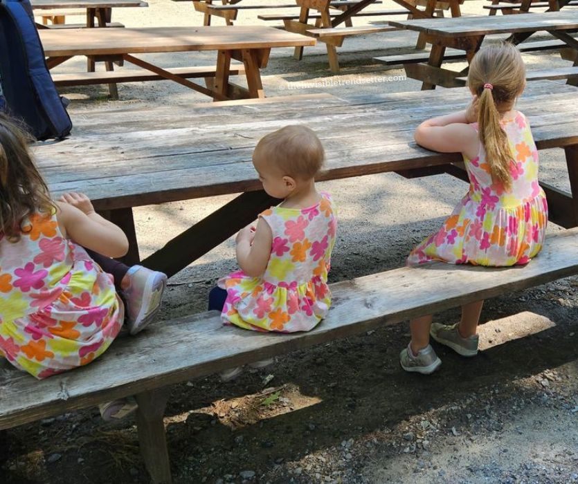Three girls in flowery dresses sitting at a picnic table.