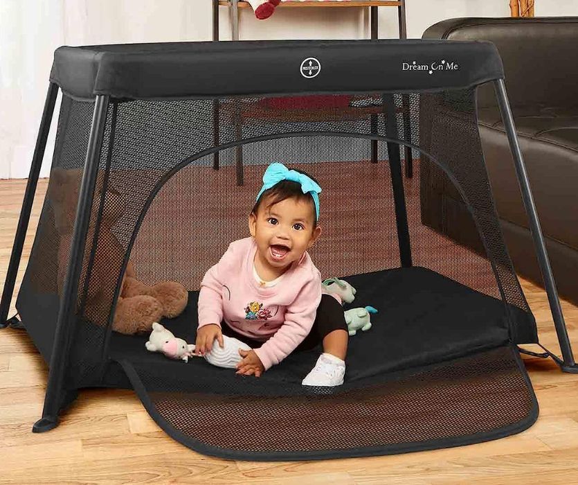 toddler sitting in a travel crib with the side zipped down