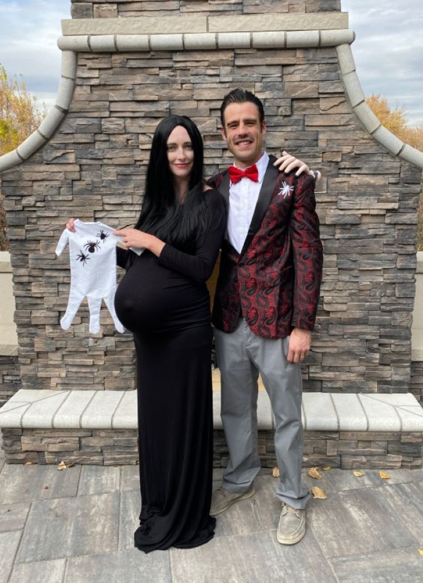 couple dressed as the addams family holding a spider baby onesie
