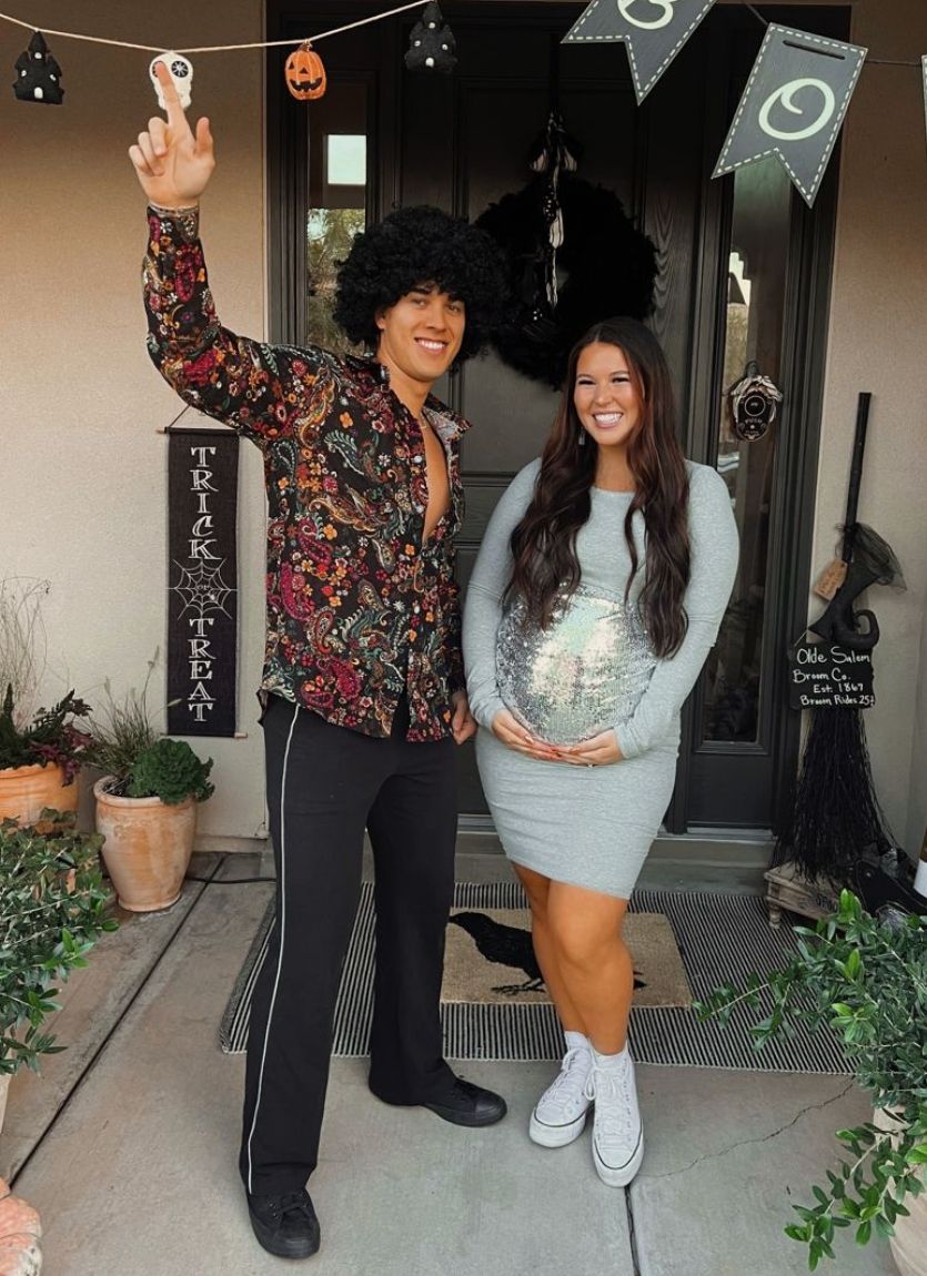 pregnant woman wearing a disco ball with a man dressed as a 70s dancer