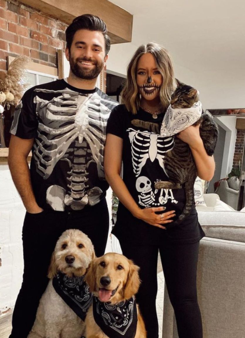 man and woman wearing skeleton halloween costumes with two dogs and a cat