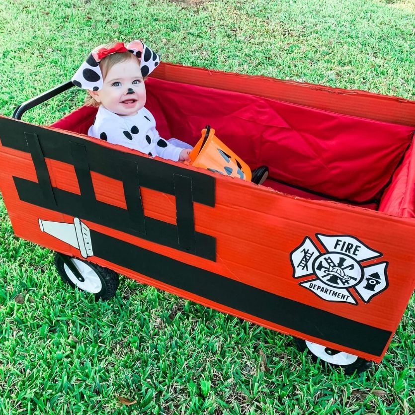 baby dressed as a Dalmatian sitting in a wagon made to look like a fire truck