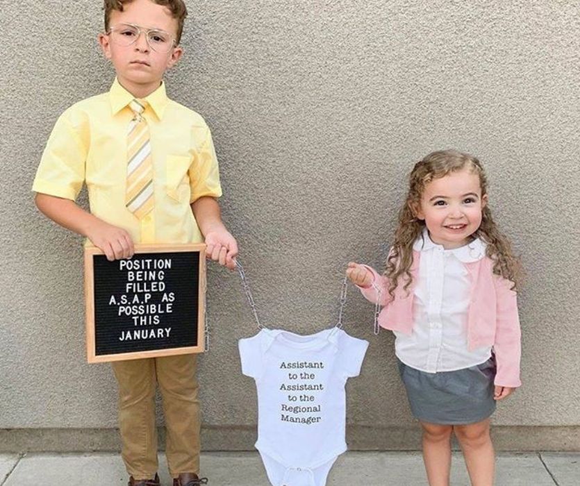 sisters dress up for halloween holding onesie for a pregnancy announcement