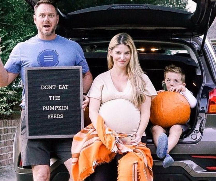pregnant woman sitting with husband and toddler holding pumpkin with a dont eat the pumpkin seeds letterboard 
