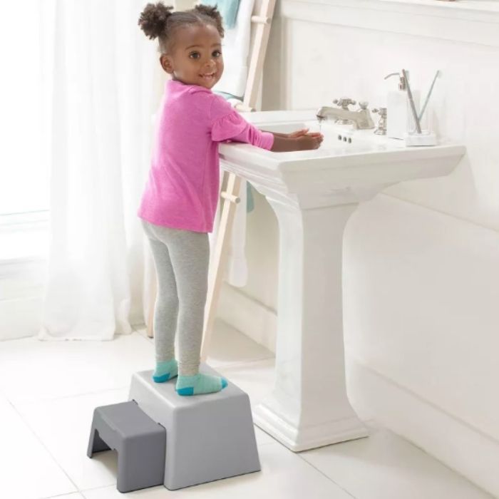 child standing on Skip Hop Double-Up Step Stool washing hands in white bathroom