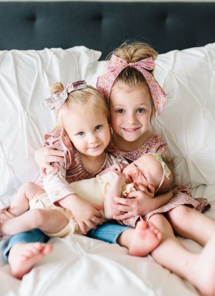 Girls holding new baby sister wearing floral bows
