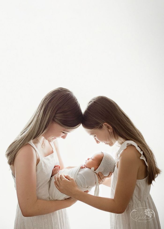 Two older sisters holding new baby sibling