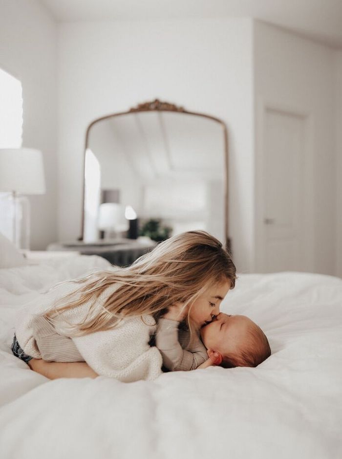 Older sister kissing new baby while laying on bed