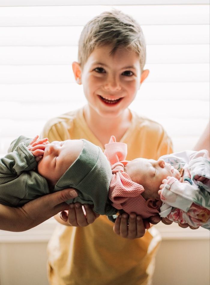 Smiling big brother with parents holding newborn twins in front of him