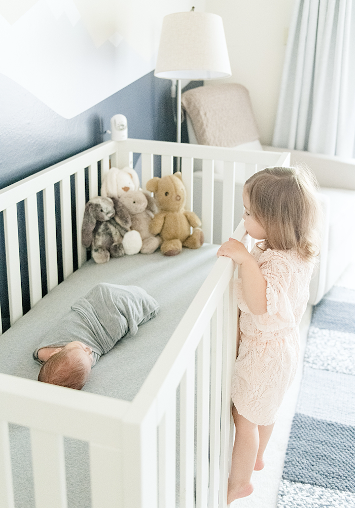 Toddler big sister climbing side of crib to see new baby sleeping