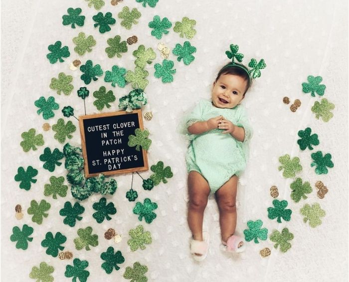 Cỏ ba lá xanh quấn quanh em bé với bảng chữ Ngày Thánh Patrick 