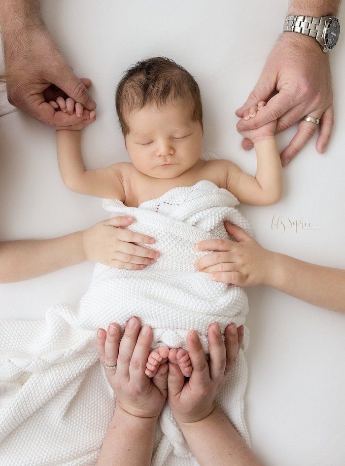 Family parents and older sibling hands on newborn baby