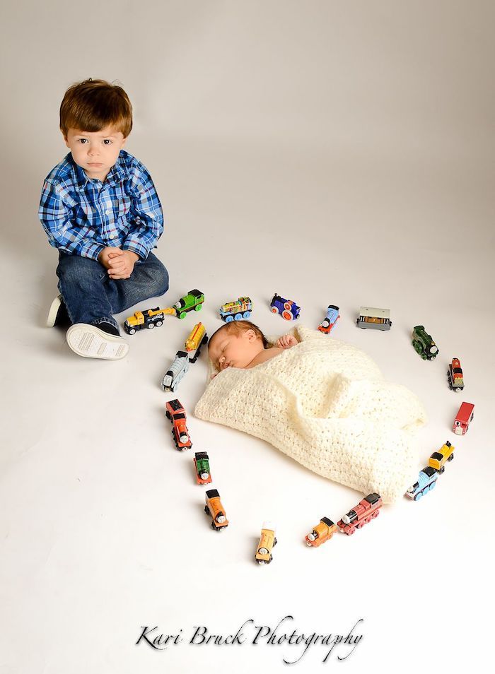 Big brother playing with toy trains in a heart around newborn baby sibling