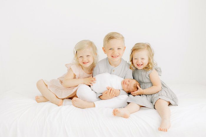 Family portrait of 3 older siblings with newborn baby
