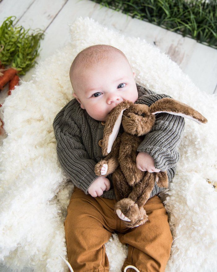 Newborn baby's first Easter photo biting stuffed bunny toy in arms