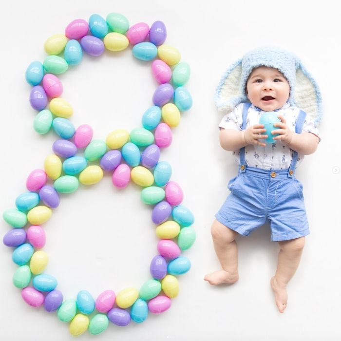 baby with bunny ear hat next to an 9 made from plastic easter eggs