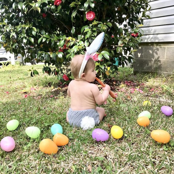 Baby's first Easter outdoor photo fluffy bunny tail and ears with bright plastic eggs on grass
