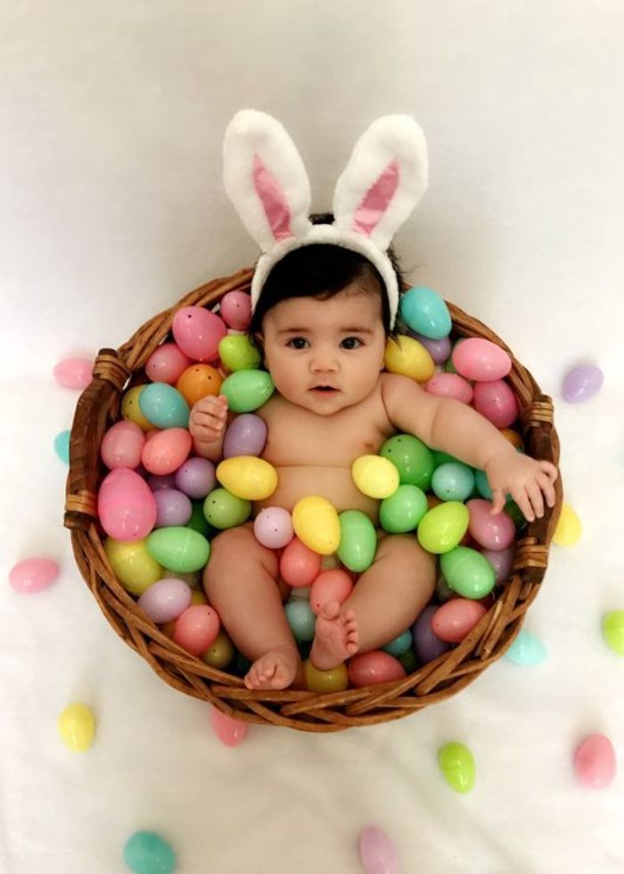 baby wearing white bunny ears in a basket full of easter eggs