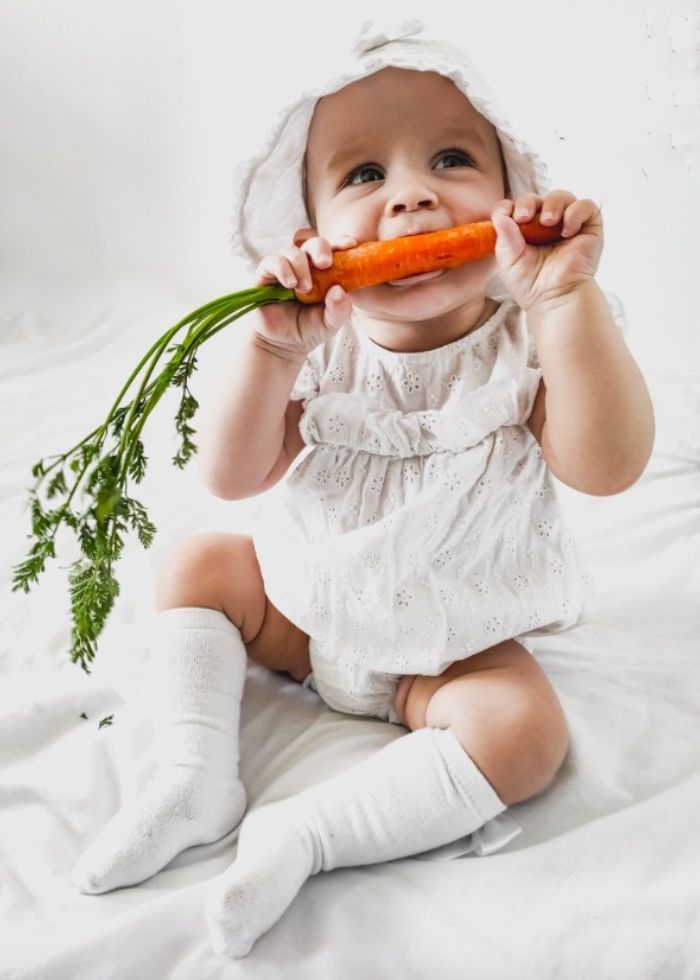 baby dressed in white holding a carrot